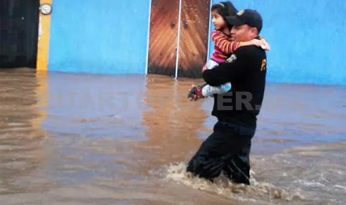 Un policía carga a una niña, cuya familia quedó atrapada en su casa, por la torrencial lluvia.