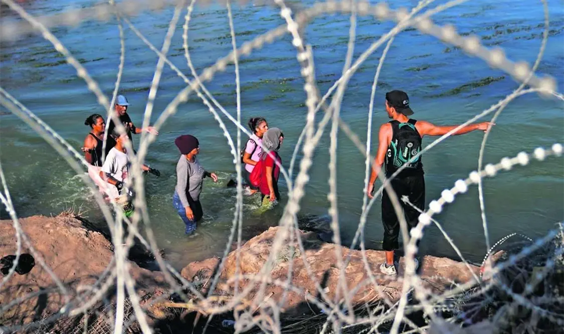 Indocumentados caminan por el río Grande a lo largo de un alambrado, mientras intentan cruzar a Estados Unidos. El Universal